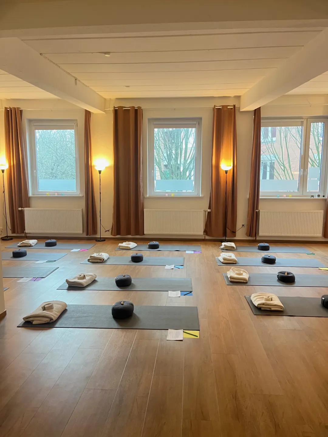 Der Raum in den Soulspaces vor dem Workshop: Yogamatten in Reihen, auf jeder eine gefaltete Decke und ein Kissen, warmes Licht von Stehlampen
